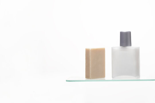 Minimalist Men's Cleansing Set: A natural bar of soap stands next to a sleek, frosted glass aftershave bottle on a transparent shelf.