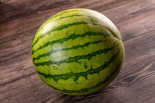 Whole fresh watermelon with green stripes on dark wooden table