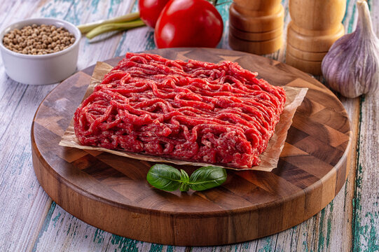 Raw ground beef on wooden cutting board with fresh vegetables and spices