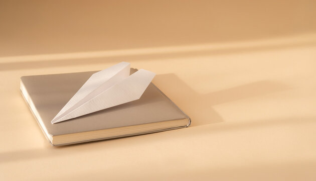 Minimalist Back to School concept with a white paper airplane on a neutral tone notebook for creativity and imagination

