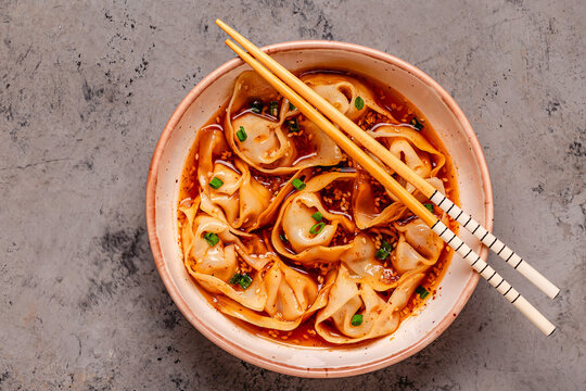 Wontons are placed in a bowl with spicy sauce.