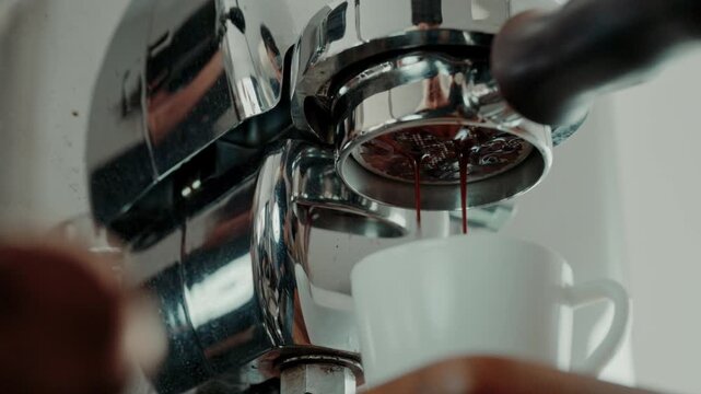 4K Pouring coffee stream from professional machine in cup. Barista man making double espresso, using filter holder. Flowing fresh ground coffee. Drinking roasted black coffee in the morning.Advertisin