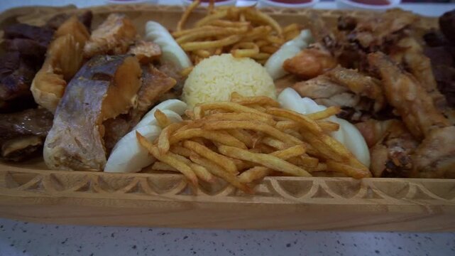 Slow motion camera panning of traditional Central Asian mixed platter with roasted meat, fried fish, french fries, and rice in a carved wooden dish, horizontal video.
