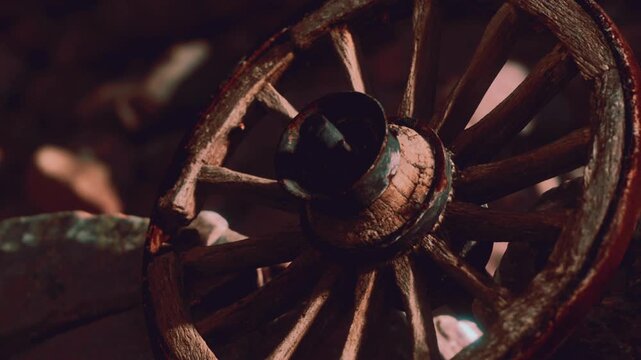 An old wooden wheel is placed on the ground near rocks at a historic site. The bright sunlight creates interesting shadows around the wheel. It shows signs of age and wear.