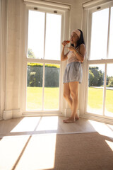 African American woman standing barefoot on wood floor by bay windows holding clear mug, copy space © wavebreak3