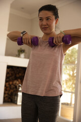 Naklejka premium African American woman in pink top lifting purple dumbbells at home by sunlit window, smartwatch