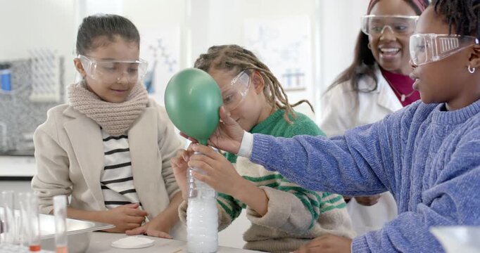 African American classmates conducting foamy bottle reaction in school lab, inflating green balloon