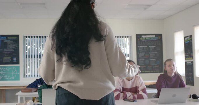Indian teacher teaching teenagers front of room after eye contact, student raising hand, laptops