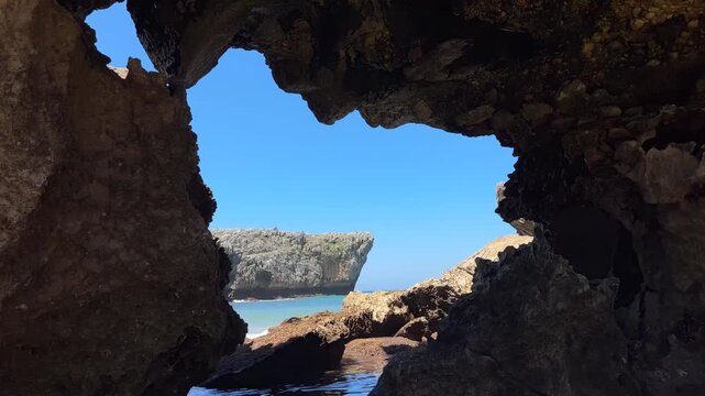 Stunning view of a rocky coastal cliff and ocean framed naturally through a dark cave opening under a clear blue sky, capturing a sense of discovery, adventure, and the rugged beauty of coastal nature