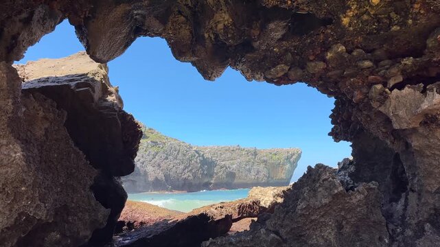 Stunning view of a rocky coastal cliff and ocean framed naturally through a dark cave opening under a clear blue sky, capturing a sense of discovery, adventure, and the rugged beauty of coastal nature