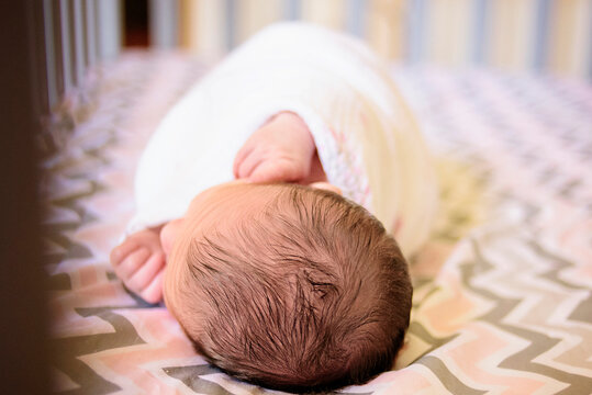 Swaddled newborn baby with dark hair sleeping peacefully