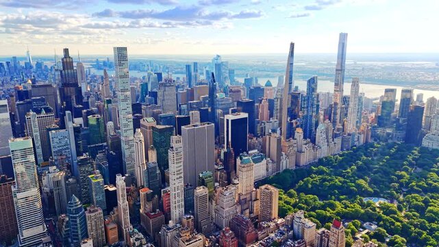 Aerial view of Manhattan skyline toward Central park south, New York City. Hudson river visible beyond towers under bright blue sky.