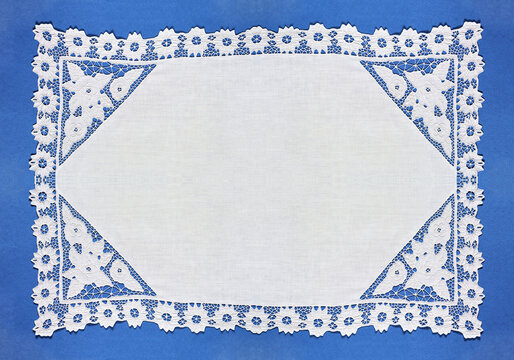 Retro white doily with openwork lace embroidery in Richelieu style with cut-out fragments on blue background. Frame with empty space for text. Closeup, top view, copy space, flat lay, blank, mockup