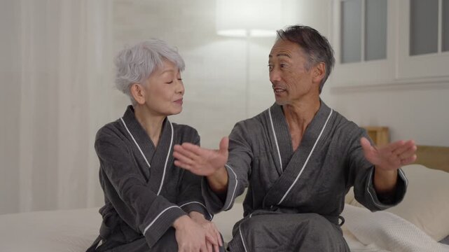 寝室にいるバスローブを着たシニア夫婦（夜）