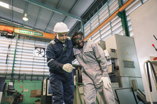 African engineer with hurting knee sitting on the floor and Caucasian worker in safety helmet helping and calling ambulance