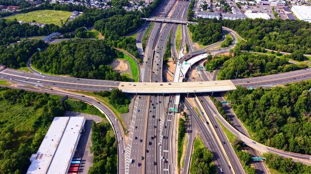 Aerial view of highway interchange near suburban town, New Jersey. Overhead drone shot of multilane roads, overpass bridge, warehouse and green tree cover. Garden state parkway