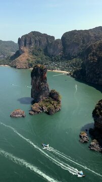 Aerial drone view of a limestone sea stack and tropical coastline near Ao Nang in Krabi, Thailand. Emerald sea, dramatic karst cliffs and speedboats in a scenic island landscape.