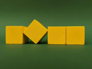 Fotobehang Lego Bright yellow cubes form a neat line on a rich green background, with one cube tilted to add dynamic balance. A playful, geometric composition perfect for design, creativity and modern decor concept  © Anida
