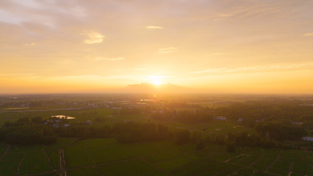 Aerial sunset panoramic view of vast rural farmland and village under golden twilight sky