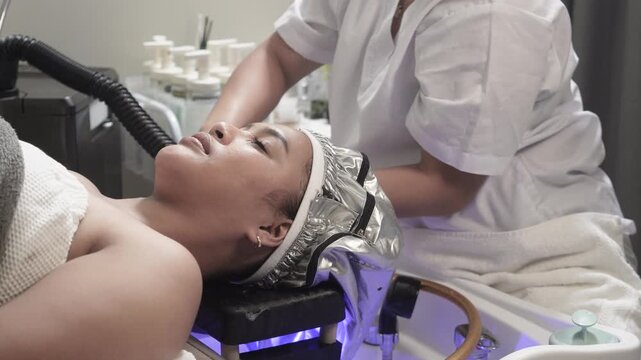 Japanese head spa therapist attaches the steamer machine hose to the heated steaming cap for deep conditioning and scalp therapy during a luxury salon treatment at japanese head spa.