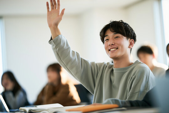 教室で笑顔で元気よく手を挙げ、質問しようとする日本人男子大学生のポートレート
