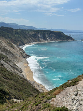 Breathtaking high-angle view of the rugged Asturian coastline in northern Spain featuring steep green cliffs, a pristine sandy beach, and turquoise ocean waves