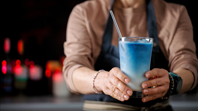 Barista serves refreshing cold blue drink with metal straw inside dim evening cafe setting