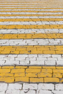 Yellow and white painted stripes cross a brick pavement