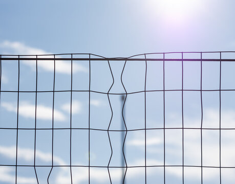 Sunlight glows behind a bent wire fence