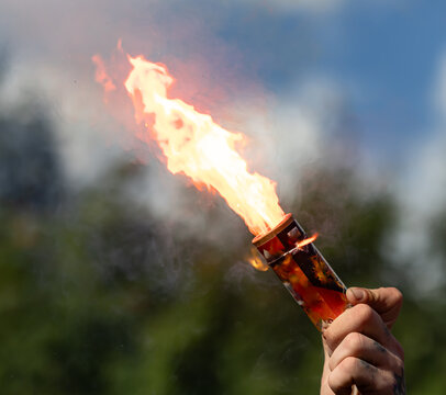 Hand holds burning torch against sky