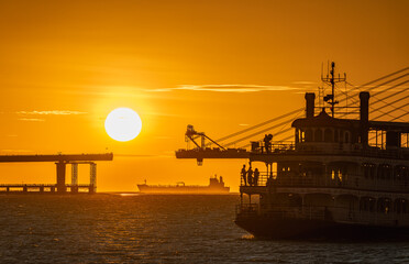 Fototapeta premium A beautiful sunset view featuring the silhouette of a ferry boat and the construction of the Danjiang Bridge in Tamsui, New Taipei City, Taiwan.