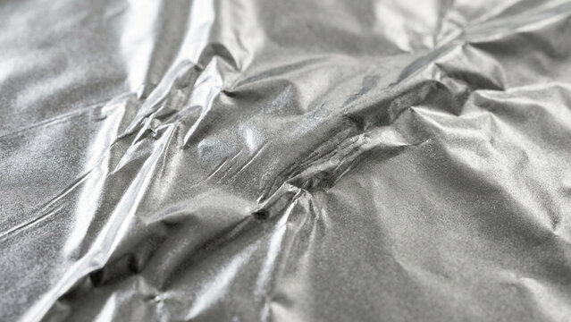 Aluminum foil displays intricate folds and metallic reflections on a textured surface.