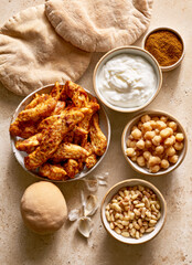 Fototapeta premium Middle eastern food ingredients with grilled chicken strips, pita bread, chickpeas, yogurt sauce, and pine nuts.