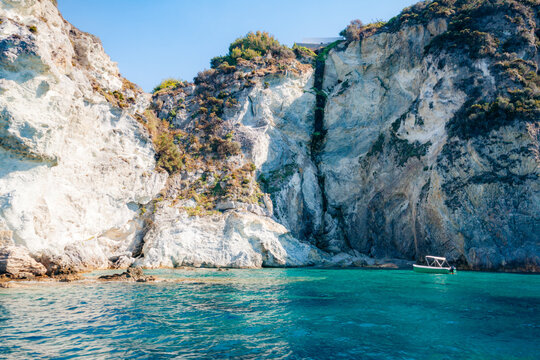 Small tourist boat cruises near the scenic white limestone cliffs of Ponza island in Italy.
