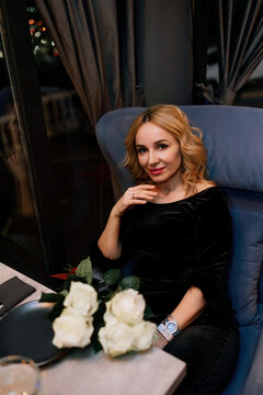 woman in a restaurant with champagne in her hand. She is sitting at a table against the backdrop of a dark restaurant hall with lamps.