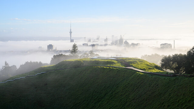 View from Mt Eden summit. Auckland Sky Tower and skyline in the fog. Mt Eden volcanic crater in the foreground. Auckland.