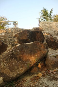 A low angle view of large brown boulders integrated into a stone retaining wall and outdoor staircase with metal railings under a clear sky