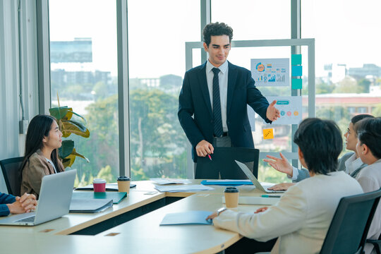 Business leader invites discussion during conference while colleagues share ideas, review presentation, analyze business performance, strengthen communication, planning, teamwork, growth.