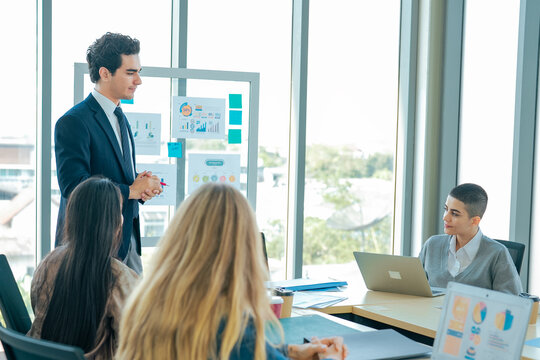 Business manager leads strategy meeting while colleagues review presentation, discuss business goals, share ideas, analyze performance metrics, improve communication, teamwork, planning.