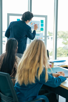 Business executive explains dashboard during conference while team reviews charts, analytics, statistics, shares insight, discusses strategy, strengthens cooperation, supports growth.