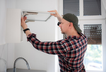 Skilled worker mounts white kitchen cupboard hardware in home during daytime maintenance project