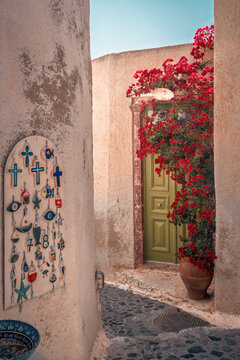 Typical greek alleyway with a green door, blooming bougainvillea, and local charms for sale