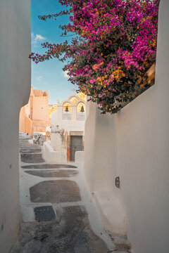 Whitewashed winding alley leading to a traditional bell tower under a bright summer sky