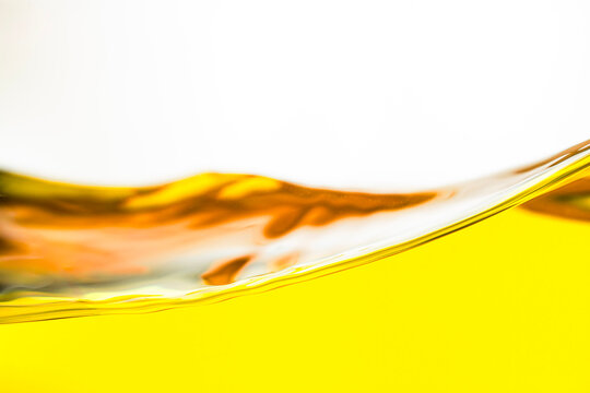 Close-up of an elegant golden oil wave with glossy reflections and smooth flowing texture on a clean white background. Minimalist composition with generous copy space, ideal for cooking oil, food, bev
