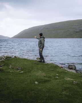 Hiker standing on the shore of Lake Leitisvatn pointing into the distance, Vagar, Faroe Islands