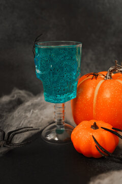 Halloween decorations include a blue drink in a skull cup with pumpkins and fake spiders on a dark table