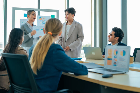 Business presenter explains financial report during meeting while colleagues review charts, discuss strategy, exchange ideas, support planning, strengthen communication, achieve shared business goals.