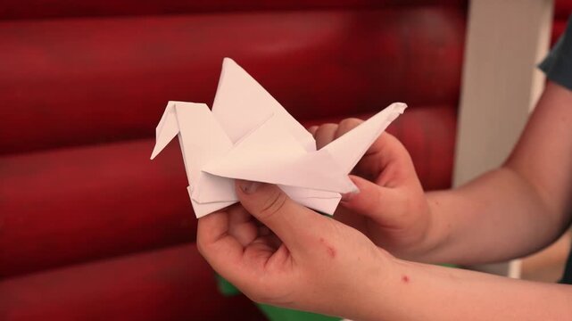 Child hands holding origami crane on red background showing Japanese cultural symbol of peace, hope and wishes with traditional paper art representing creativity, purity and meaningful heritage