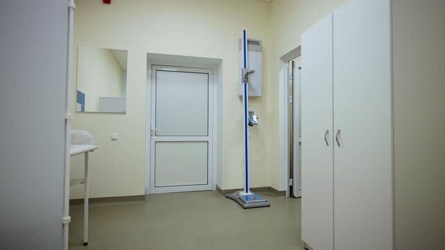 Medical office contains tall wardrobe stadiometer scale and privacy panel. Sterile clean layout creates highly professional clinic mood