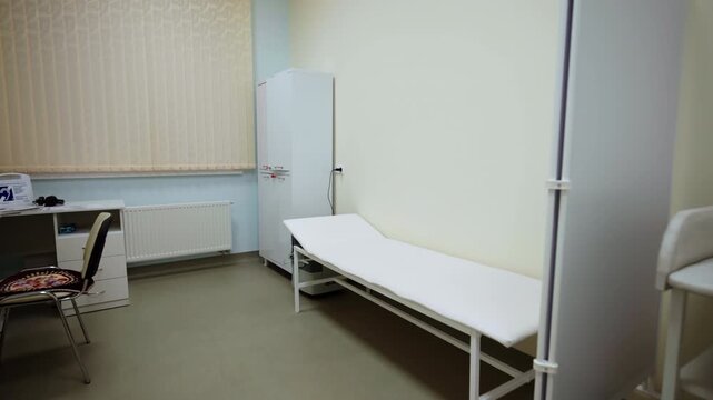 Medical room features empty examination couch privacy screen and changing table. Sterile interior creates quiet mood for patient checkups
